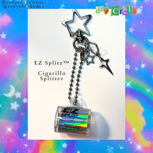 May include: A silver keychain with a star charm and a clear plastic cylinder with the text "EZ Splitz™ Cigarillo Splitter" and a warning label. The keychain is hanging from a silver chain.