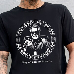 Peut inclure: T-shirt noir avec un graphique blanc d'un homme avec une barbe et des lunettes de soleil. Le graphique est à l'intérieur d'un cercle avec le texte "Je ne teste pas toujours mon code, mais quand je le fais, c'est en production." et "Restez au téléphone mes amis".
