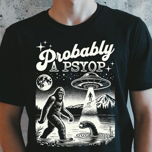 May include: Black t-shirt with a white graphic design featuring a Bigfoot, a UFO, and the text "Probably a PSYOP".