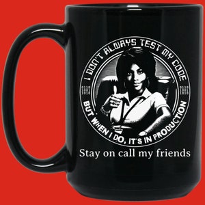 May include: Black ceramic mug with a large handle. The mug features a black and white graphic of a woman giving a thumbs up, surrounded by text that reads "I DON'T ALWAYS TEST MY CODE BUT WHEN I DO, IT'S IN PRODUCTION. Stay on call my friends."