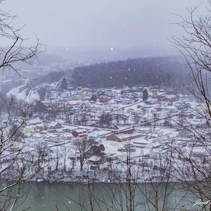 Centro del Carbón - Chubasco de nieve sobre Newell enmarcado entre árboles desde Highpoint Drive en una tarde de enero