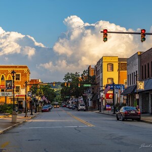 May include: A street scene in a small town with brick buildings, a McDonald's restaurant, and a sign that reads "Fourth St.". The street is lined with trees and there are cars parked on both sides. The sky is blue with white clouds.