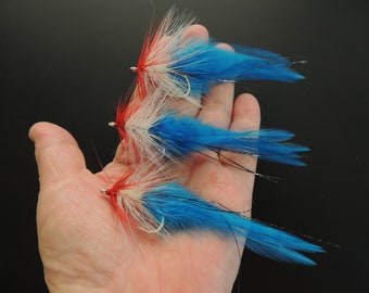 May include: Three fly fishing lures with red, white, and blue feathers. The lures are tied on hooks with silver rings.
