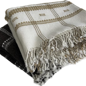 May include: Two folded blankets. One is white with a brown grid pattern and fringe. The other is black with a white grid pattern. The blankets are made of a woven material.