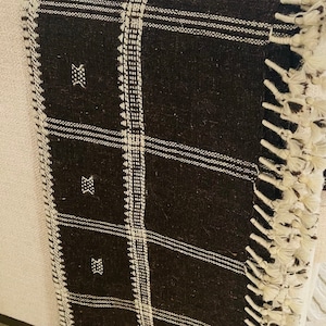 May include: Black and white striped throw blanket with fringe. The blanket has a geometric pattern and is made of a soft, woven fabric.