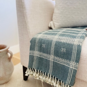 May include: A blue and white plaid throw blanket with fringe on a white couch. The blanket has a subtle pattern of small white stars.