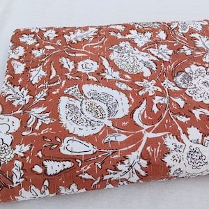 May include: A rust-colored kantha quilt with a white floral pattern. The quilt is made of cotton and has a hand-stitched design.