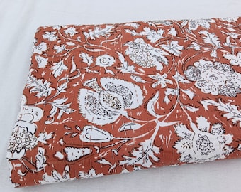 Puede incluir: Una colcha kantha de color óxido con un patrón floral blanco. La colcha está hecha de algodón y tiene un diseño cosido a mano.