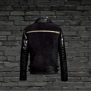 May include: Black leather jacket with crocodile-embossed sleeves and a gold zipper. The jacket has a suede-like texture and a black background.