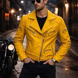 Front view of a handmade yellow leather biker jacket featuring a cropped moto silhouette with bold gold zipper detailing. Crafted from genuine leather, the jacket includes an asymmetrical zip closure, multiple zip pockets, and a structured fit designed to stand out. Styled on a male model outdoors in an urban night setting beside a motorcycle to highlight vibrant color, craftsmanship, and statement appeal for modern moto and leather fashion buyers.