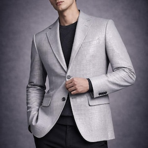 May include: A light grey blazer featuring a textured crocodile skin pattern, a notched lapel, two front buttons, and two flap pockets. The blazer is worn over a dark charcoal grey sweater and paired with black trousers.