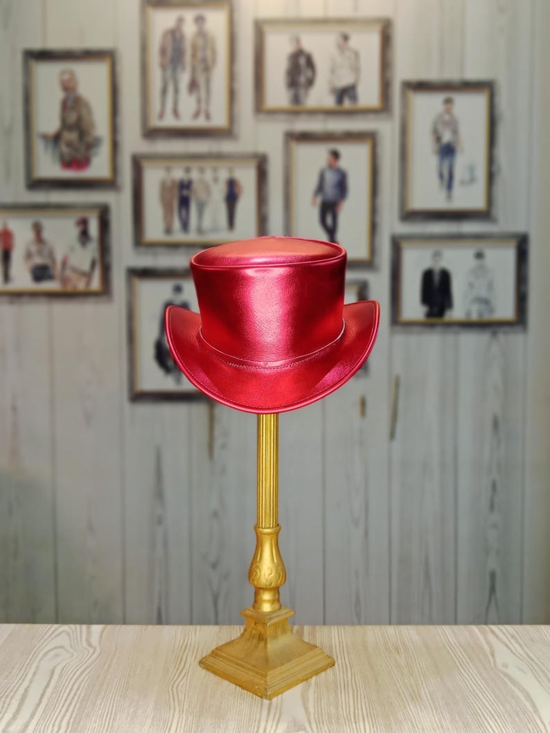 May include: A bright red top hat with a shiny finish sits on a gold stand. The hat is made of leather and has a wide brim.