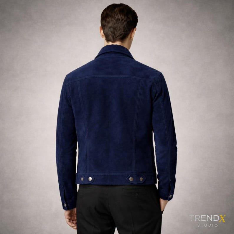 May include: A navy blue suede jacket with a classic collar and buttoned cuffs. The jacket has two chest pockets and a button closure. The model is wearing black trousers. A stylish outerwear piece.