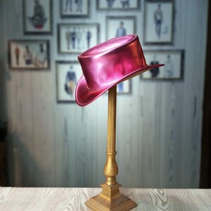 May include: A bright pink top hat with a shiny finish sits on a gold stand. The hat is made of a smooth, glossy material.
