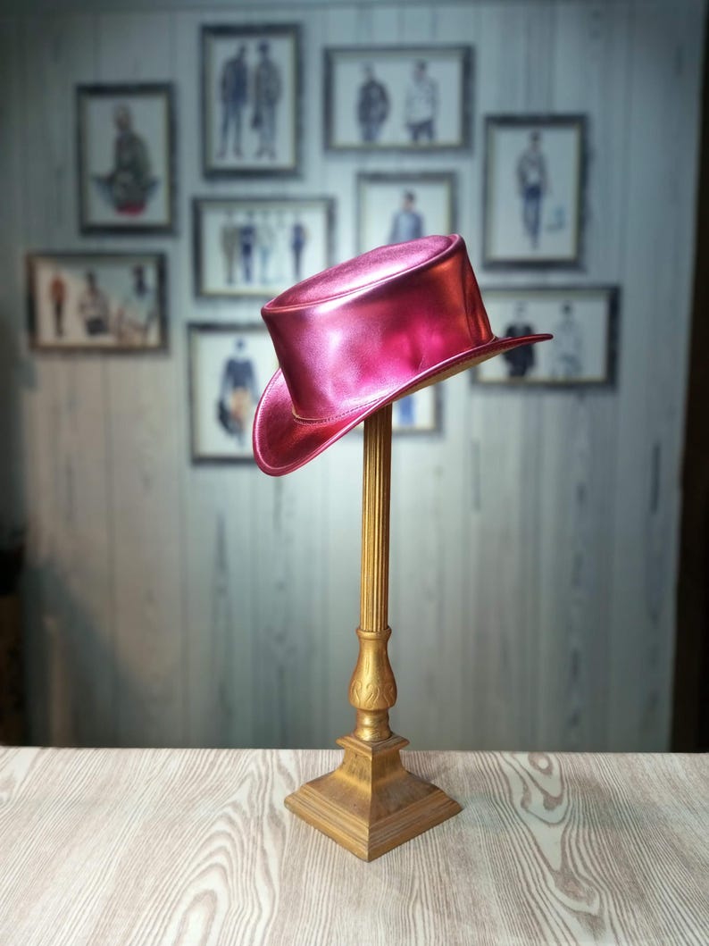 May include: A bright pink top hat with a shiny finish sits on a gold stand. The hat is made of a smooth, glossy material.