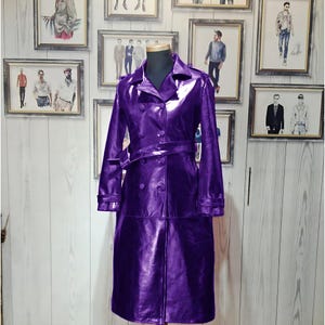 Può includere: Un lungo trench in pelle lucida di colore viola, con chiusura a doppio petto e cintura.