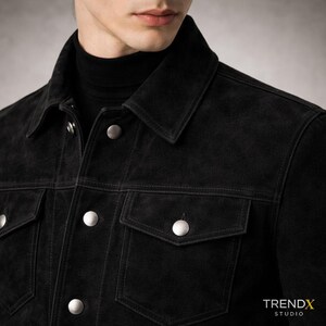 May include: A black suede jacket with silver buttons and two chest pockets. The jacket has a classic collar and is worn over a black turtleneck. The image is from TRENDX STUDIO.