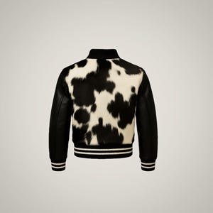 以下が含まれることがあります： 白と黒の牛革ボンバージャケット。背面パネルは天然の牛革模様で、袖と襟は黒です。袖口と裾には白いストライプが入っています。スタイリッシュなアウターウェアです。
