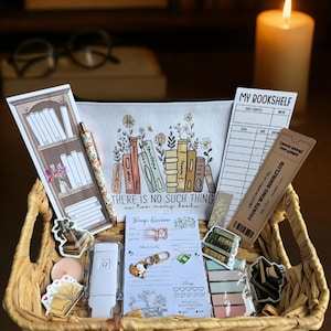 Könnte beinhalten: Eine Sammlung von Artikeln zum Thema Bücher in einem Weidenkorb. Enthält ein Federmäppchen mit Blumen- und Buchdesign, Aufkleber, Lesezeichen, einen Stift und einen Buchbesprechungsbogen. Auf dem Federmäppchen steht "THERE IS NO SUCH THING as too many books."