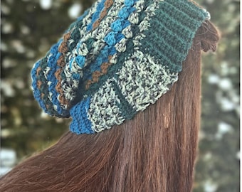 May include: A crochet beanie featuring a textured pattern with horizontal stripes in shades of dark green, teal, light blue, and brown. The hat has a ribbed brim and a slouchy fit, constructed with varied yarn weights and stitch densities throughout.