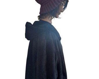 May include: A dark purple crocheted beanie with a thick ribbed cuff and a textured, bobble-like stitch pattern. The beanie is worn on a head, paired with a black hooded garment that features a soft, plush, and velvety fabric texture.