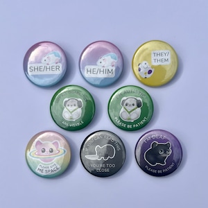 Peut inclure: Ensemble de neuf badges ronds avec différents motifs et messages. Les badges présentent des animaux de dessin animé et du texte tel que "She/Her", "He/Him", "They/Them", "Je suis autiste, s'il vous plaît soyez patient", "Toutes les incapacités ne sont pas visibles", "Si vous pouvez lire ceci, vous êtes trop près", "Je suis sourd, s'il vous plaît soyez patient", et "S'il vous plaît, donnez-moi de l'espace".