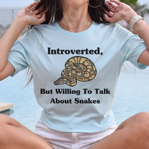May include: A light blue t-shirt with the text "Introverted, But Willing To Talk About Snakes" and a cartoon image of a snake.