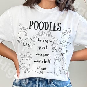 May include: White t-shirt with the word "POODLES" in black, along with a graphic of poodles and the text "The dog so great everyone wants half of one." The shirt has a crew neck and short sleeves.
