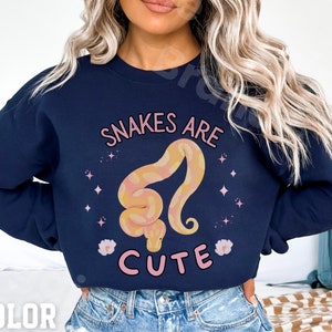 May include: Navy blue sweatshirt featuring a pink and yellow snake graphic with the text "Snakes are cute".
