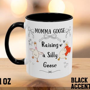 以下が含まれることがあります： 黒いハンドルと縁が付いた白いセラミックマグ。マグには「Momma Goose Raising a Silly Goose」のテキストとガチョウのイラストが描かれています。マグは325mlです。