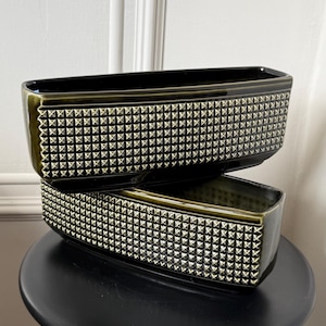 May include: Two rectangular ceramic planters with a dark olive green glaze and a textured exterior featuring a repeating grid of raised pyramid studs. The planters have a smooth, glossy finish and a deep, open interior cavity for holding items.