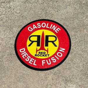 May include: A red and yellow round sticker with the words "GASOLINE DIESEL FUSION" around the edge. In the center is a yellow circle with a black "RR" logo and a red rocket ship with the words "RED ROCKET" underneath.