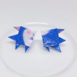 May include: A pair of blue origami earrings with white and pink accents. The earrings are folded into a geometric shape.