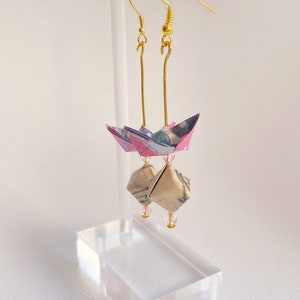 May include: A pair of gold origami earrings with pink and blue paper cranes and pink beads hanging from the bottom.