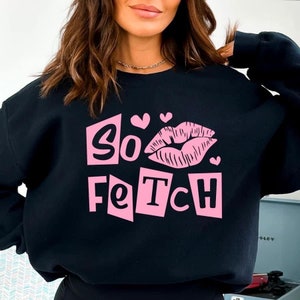 Może przedstawiać: Czarna bluza z różowym nadrukiem graficznym, na którym widnieje napis "So Fetch" wraz z różowym nadrukiem ust i serduszkami.
