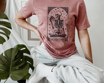 May include: A heather mauve t-shirt with a graphic of a skeleton eating a slice of pizza. The graphic is surrounded by hearts and stars. The text "The Pizza Lover" is below the graphic.