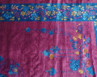 Può includere: Un tappeto vintage con sfondo bordeaux scuro e un bordo floreale blu e oro. Il tappeto presenta un motivo floreale ripetitivo in tonalità blu e oro.