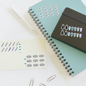 May include: A set of science-themed stickers featuring beakers, test tubes, petri dishes, and pipettes. The stickers are on a light blue notebook and a beige card.