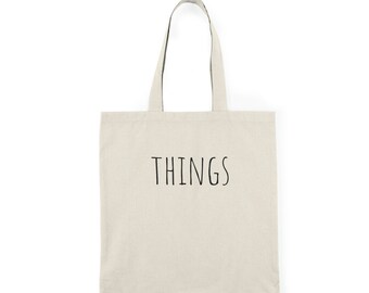 Könnte beinhalten: Eine beige Canvas-Tragetasche mit schwarzen Henkeln und dem Wort "THINGS" in Schwarz auf der Vorderseite.