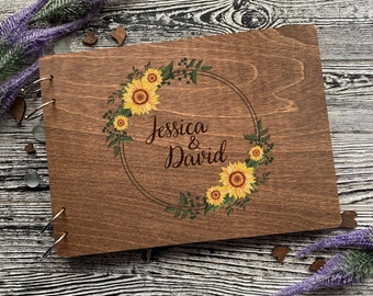Könnte beinhalten: Ein Holzfotoalbum mit einem Sonnenblumenkranz-Design und den Namen "Jessica & David" auf der Vorderseite.