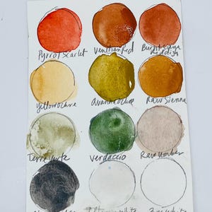 May include: Watercolor paint color swatches on a white paper. The colors include Pyrrol Scarlet, Venetian Red, Burnt Sienna, Yellow Ochre, Avenncochre, Raw Sienna, Terre Verte, Verdaccio, Raw Umber, Black Ochre, Titanium White, and Zinc White.