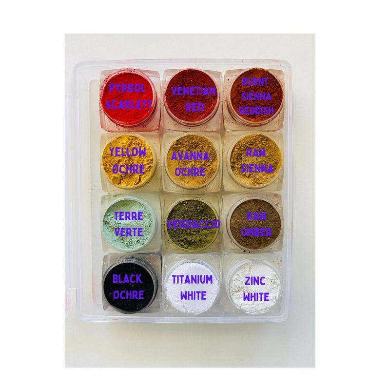 May include: A clear plastic container holding twelve small jars of artist pigments. The jars are labeled with color names like "Pyrrol Scarlet", "Venetian Red", "Burnt Sienna Reddish", "Yellow Ochre", "Avanna Ochre", "Raw Sienna Vienna", "Terre Verte", "Green Oxide", "Raw Umber", "Black Ochre", "Titanium White", and "Zinc White".