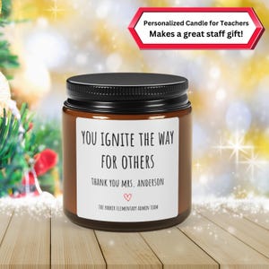 May include: A brown glass candle with a black lid and a white label that reads "You ignite the way for others. Thank you Mrs. Anderson. The Parker Elementary Admin Team." The label has a small red heart.