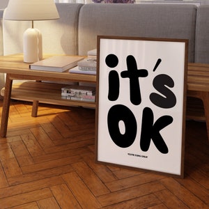 May include: A framed black and white poster with the text "it's ok" in large, bold, black letters. The text "you're doing great" is printed in smaller letters below the main text.