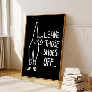 May include: Black and white illustration of a cat with the text "Leave those shoes off..." on a black background.