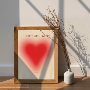 May include: A framed print with a red heart and the text "FIRST, SELF LOVE" in black. The text "DON'T FORGET" is in smaller font below the heart.