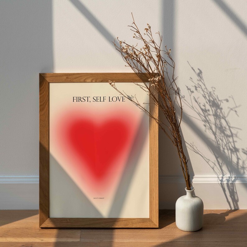 May include: A framed print with a red heart and the text "FIRST, SELF LOVE" in black. The text "DON'T FORGET" is in smaller font below the heart.