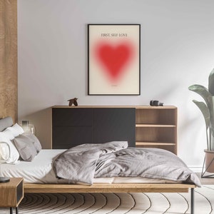 May include: A bedroom interior with a bed, a wooden nightstand, a lamp, a dresser, a plant, and a framed print with a red heart and the text "FIRST, SELF LOVE".