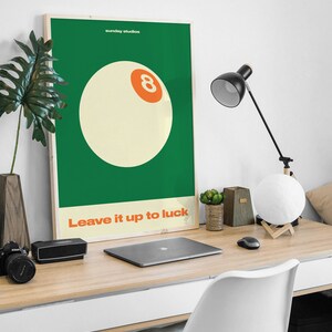May include: A green and white poster with the text "sunday studios" and "Leave it up to luck". A white billiard ball with an orange number eight is in the center of the poster.