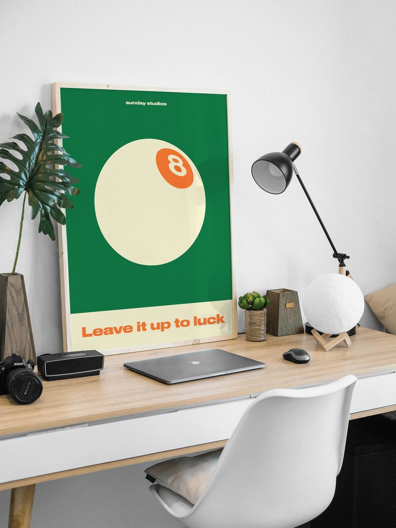 May include: A green and white poster with the text "sunday studios" and "Leave it up to luck". A white billiard ball with an orange number eight is in the center of the poster.